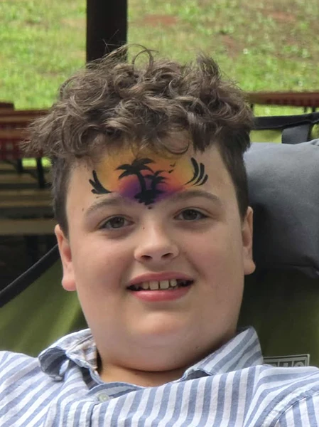 Young person smiling with forehead face paint of a sunset island scene