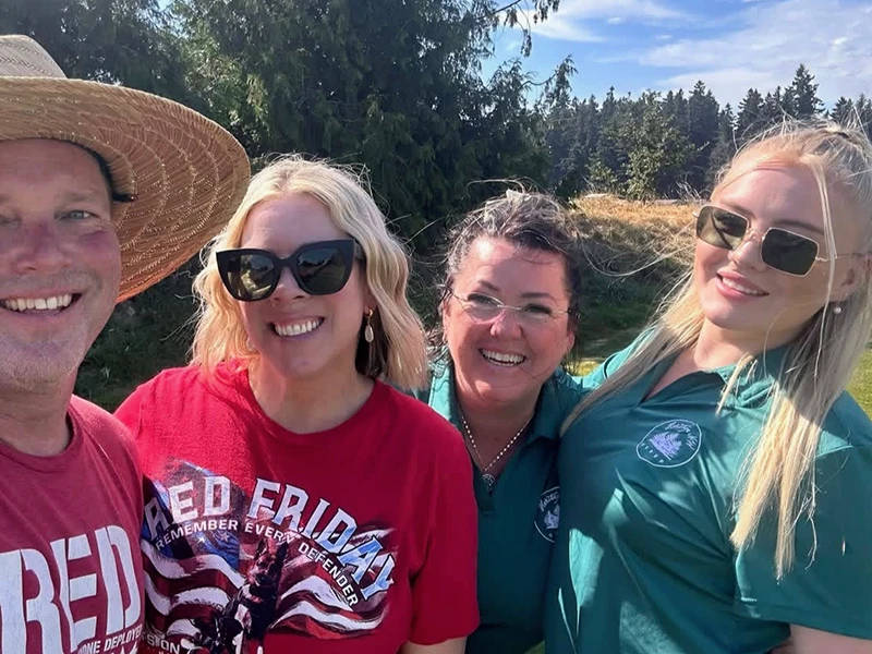 Tara and Eryn, wearing Heritage NW Group green shirts pose for a group selfie with people wearing Red Friday shirts.