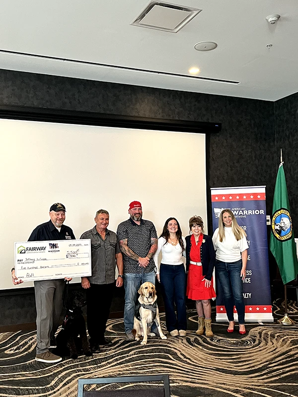 AWI presents service dogs to veterans. One person holds a giant check.