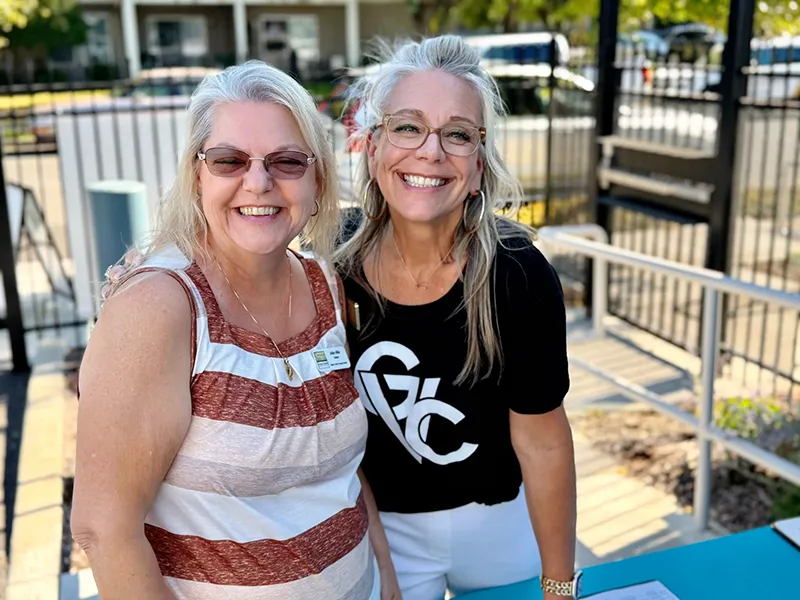 Two people stand together outside and smile. One is wearing a black GVC shirt.