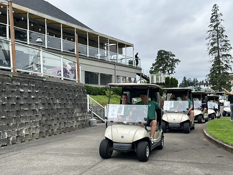 A line of golf carts, lead by the two Team Heritage carts carrying our golf team