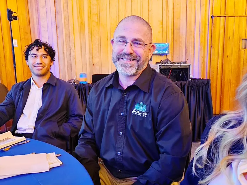 A Heritage employee wearing a black shirt with Heritage NW logo embroidered on it sits at a table.