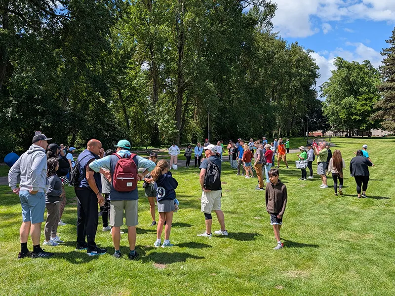 A green grassy area surrounded by trees is full of people who have gathered for the NAMIWalk.