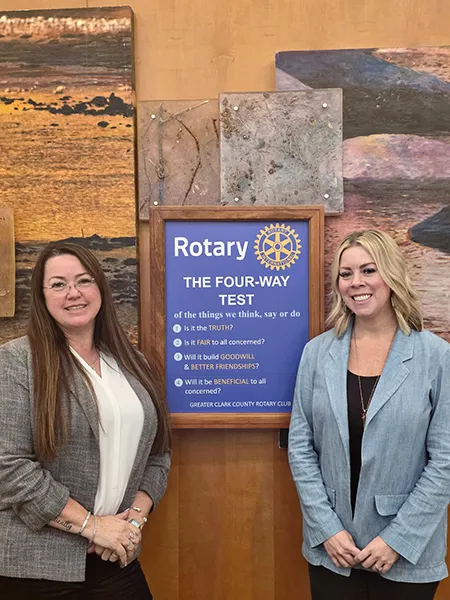 Tara and another woman stand beside a sign that says: Rotary, The four-way test of the things we think, say or do. 1. Is it the truth? 2. Is it fair to all concerned? 3. Will it build goodwill and better friendships? 4. Will it be beneficial to all concerned? Greater Clark County Rotary Club
