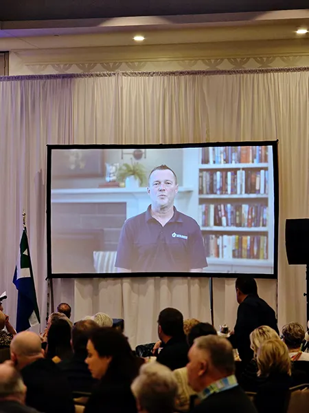 A screen showing a video to a room full of people.