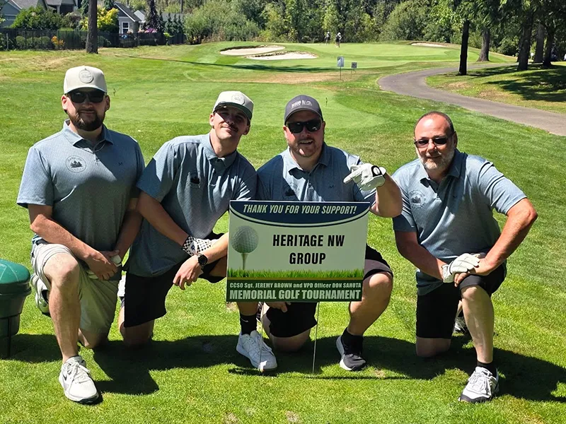 Heritage employee golf team kneel on the golf course behind the Heritage NW Group thank you for your support sign.
