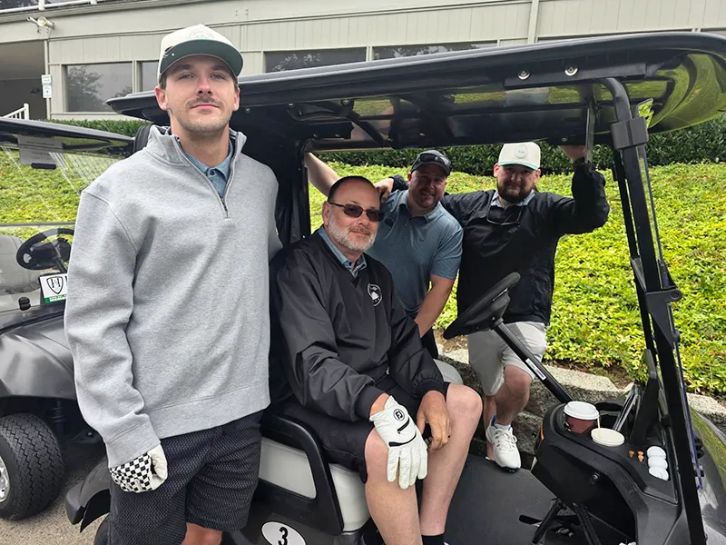 The Heritage NW golf team are gathered in and around the golf cart, ready for the tournament.