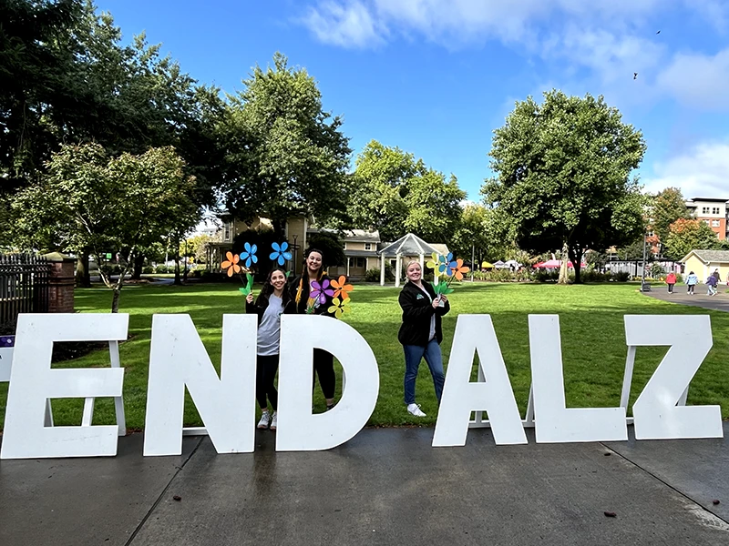 Large white letters that say END ALZ propped up on a sidewalk. Heritage employees stand behind the letters holding flowers