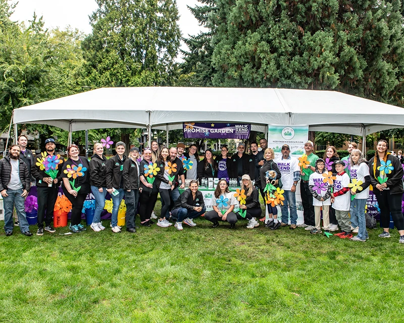 Heritage NW Group employees and family gathered in front of a booth holding flowers representing participant's connection to Alzheimer's disease.