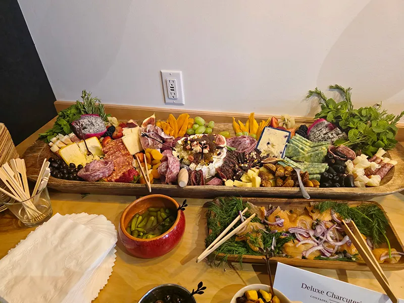 A deluxe charcuterie board with meats, cheeses, herbs, olives, pickles, onions and fruits.