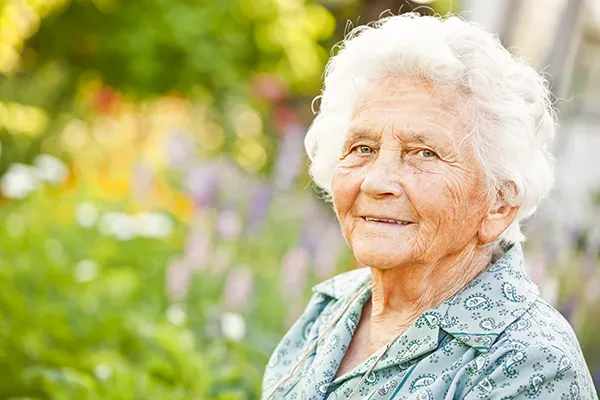 person with white hair wearing blue collared shirt smiling with a blurred background of garden flowers
